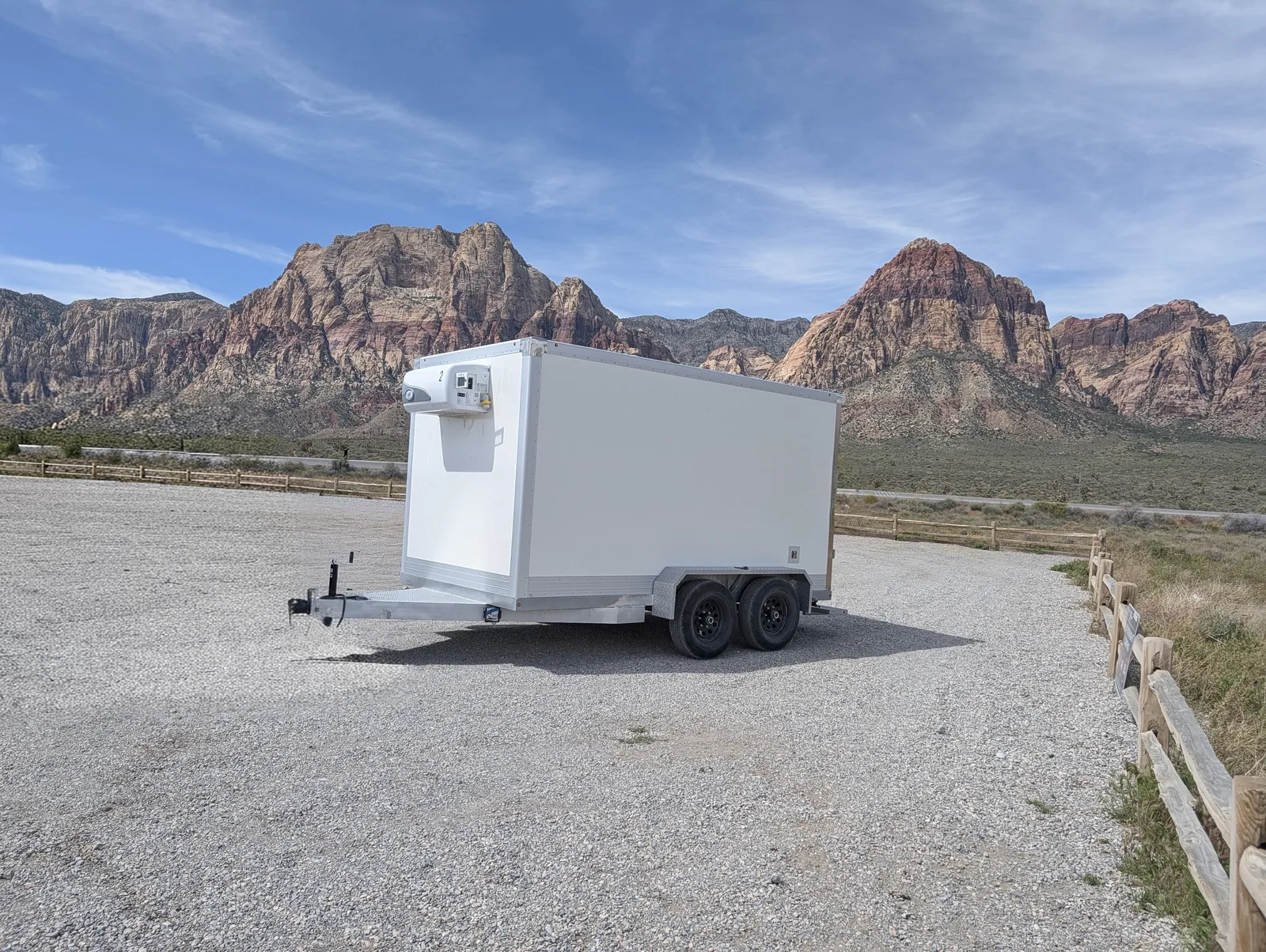White RTD refrigerated trailer with a nose-mounted cooling unit parked on gravel in front of red rock mountains