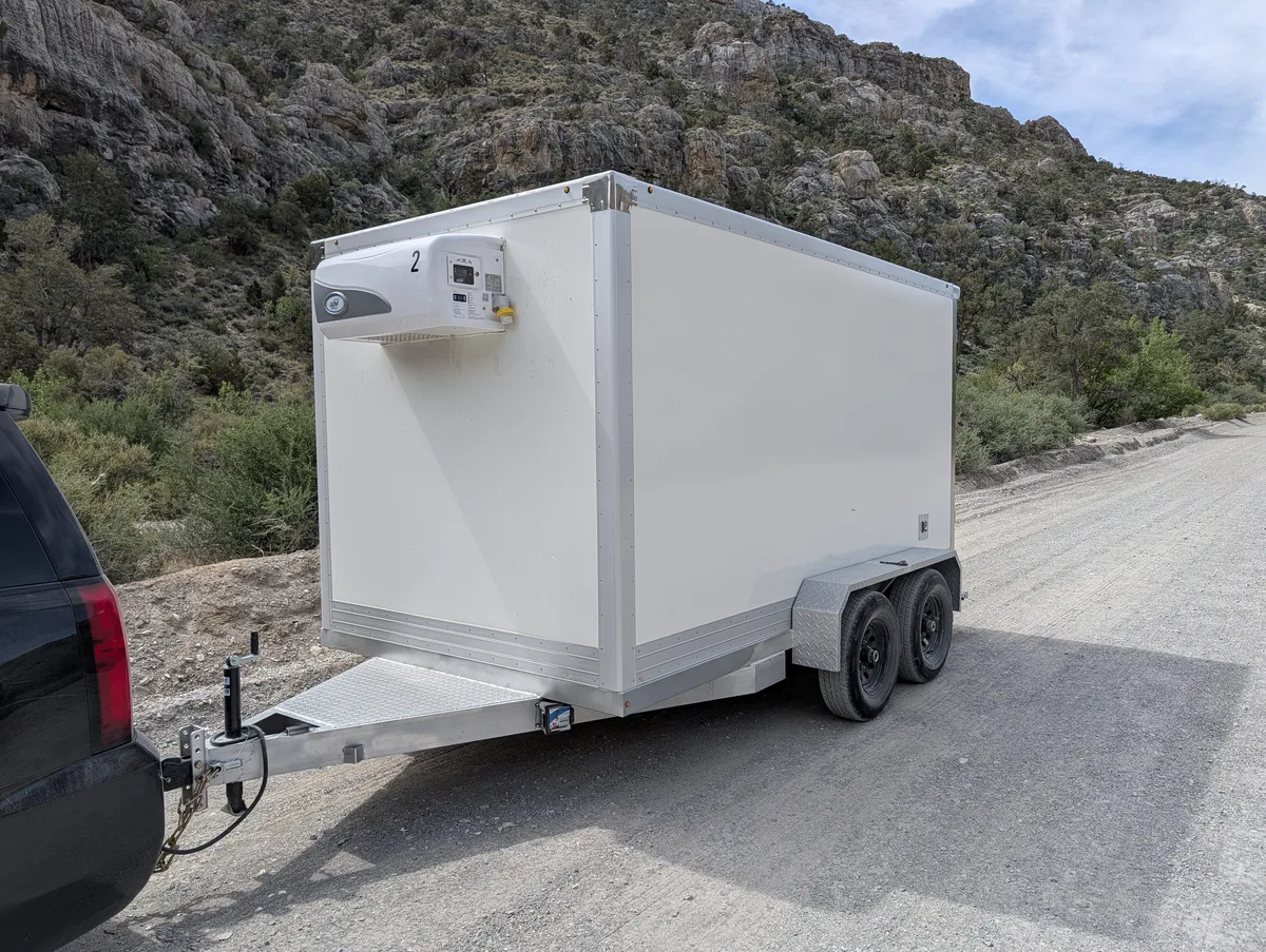 Refrigerated trailer hitched to a black full-size SUV on a canyon road